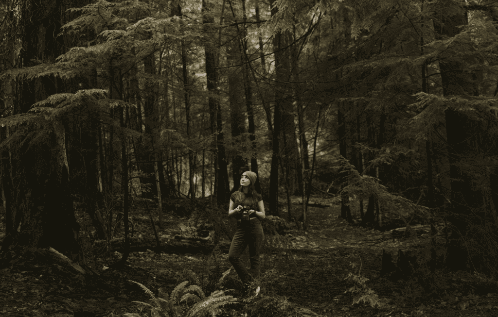 Washington wedding photographer holding her camera while exploring a lush Pacific Northwest forest.