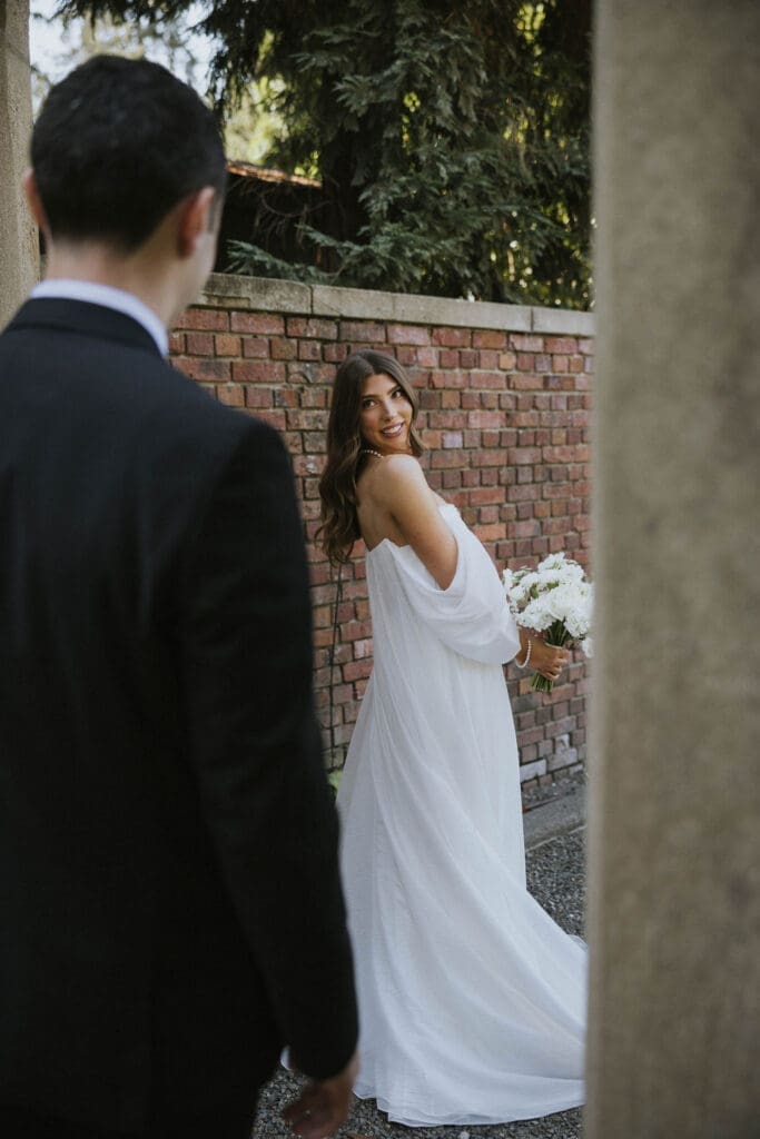 Bride holding a white flower bouquet and looking back at the groom during their Washington wedding.