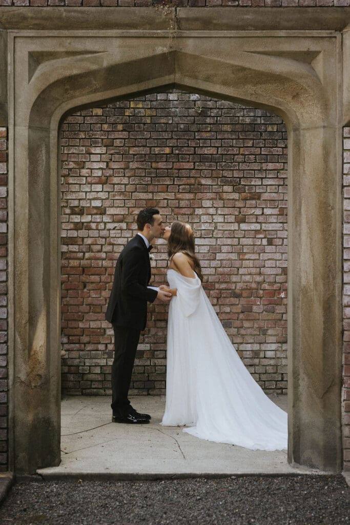Bride and groom kissing beneath a historic stone archway during their Washington estate wedding.