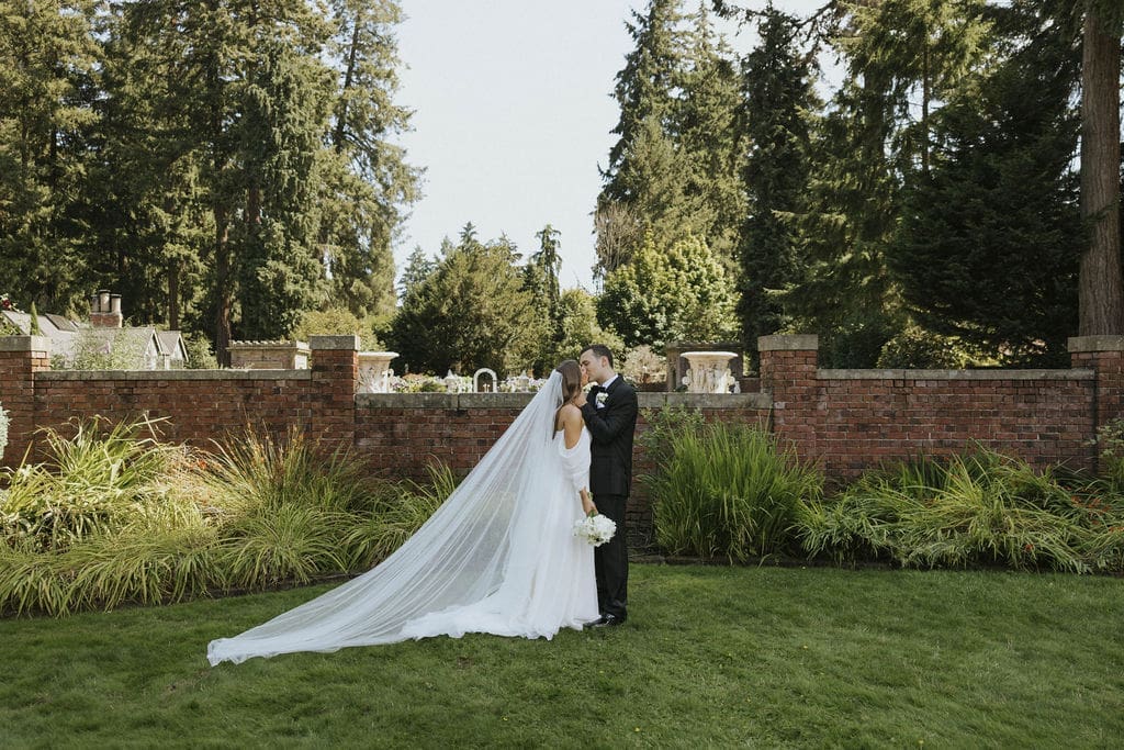 Bride and groom kissing in a lush garden with the bride’s long veil flowing behind her at an elegant Washington estate wedding.