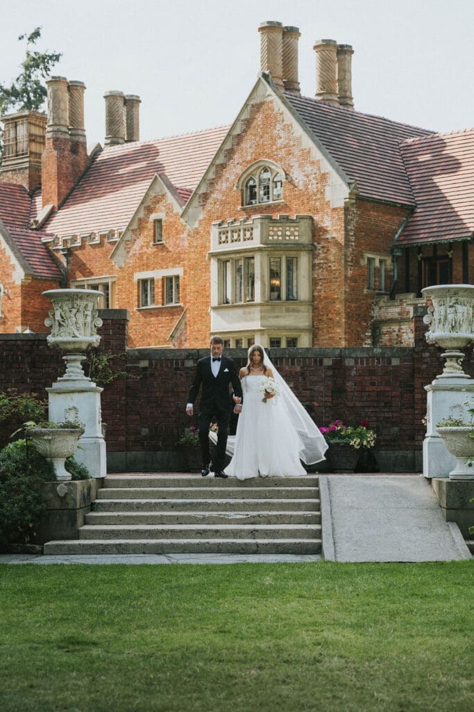 Bride and groom walking down the steps of a historic brick estate after their outdoor Washington wedding ceremony.