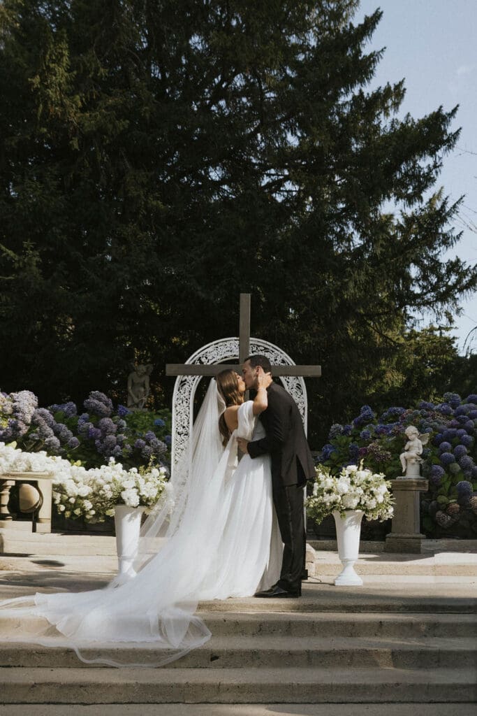 Bride and groom sharing their first kiss surrounded by hydrangeas during a romantic Washington estate wedding ceremony.
