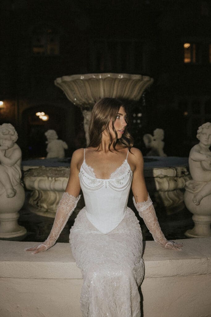 Editorial bridal portrait in a lace wedding dress beside an ornate fountain at a historic Washington estate wedding venue.