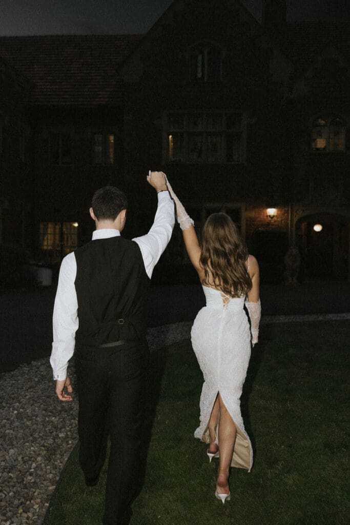 Bride and groom walking hand in hand toward a historic estate at night after their Washington wedding celebration.